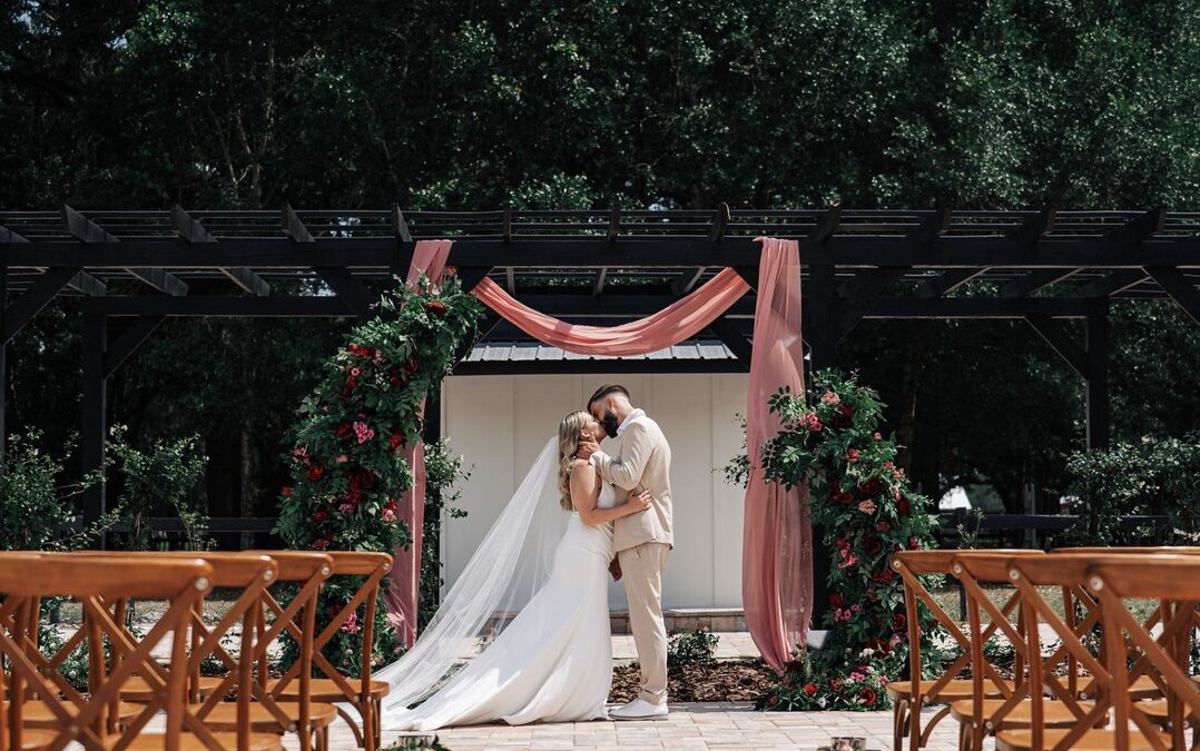 Bride and groom kissing under a rustic outdoor ceremony arch decorated