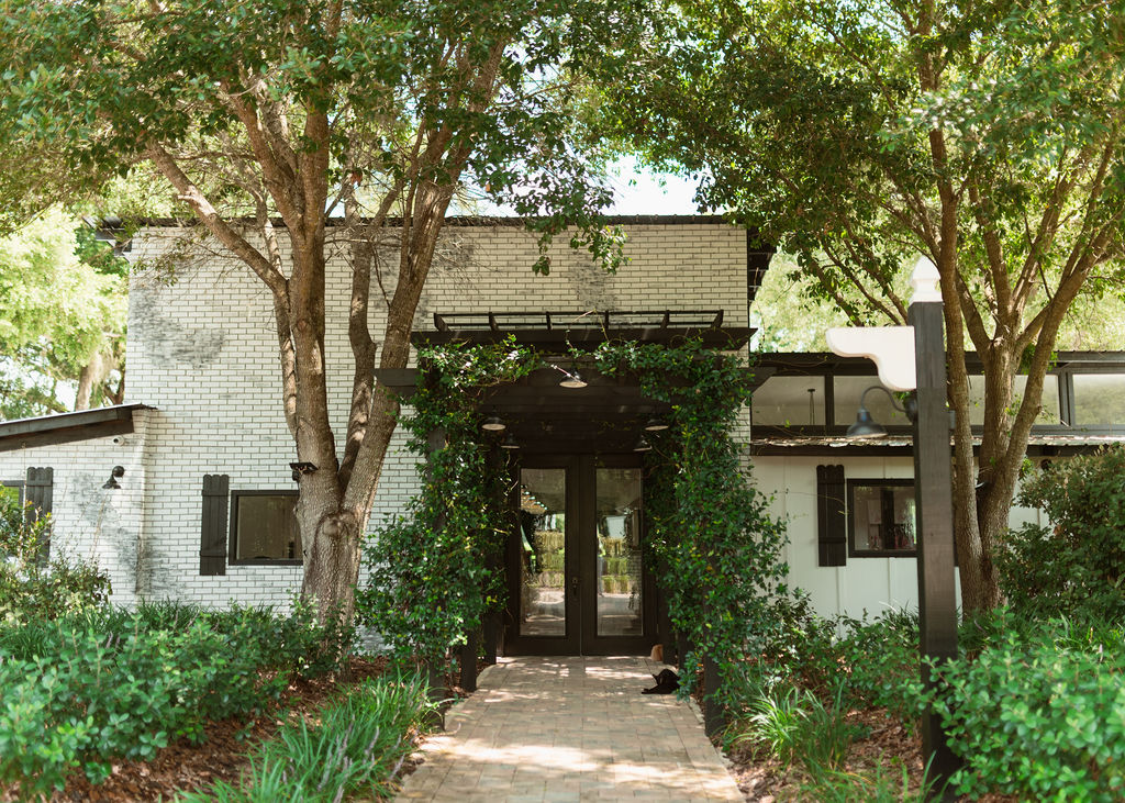 Front entrance of Villa Serafina featuring a tree-lined brick walkway, ivy-covered pergola, and modern white brick exterior.